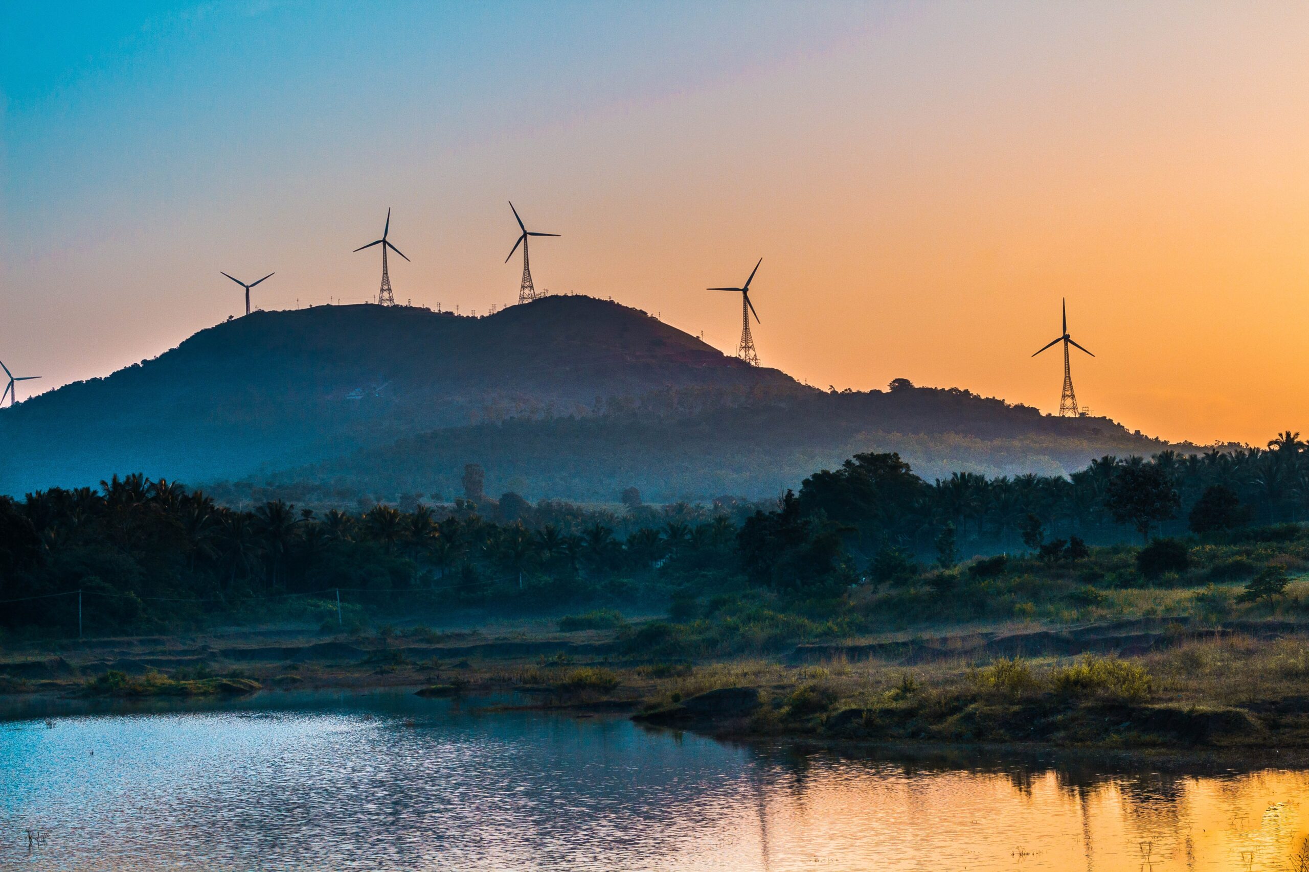 Sunset view of a mountain with windmills on top by the water